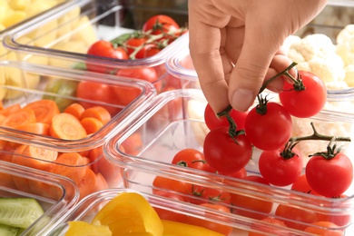Photo of Woman putting tomatoes into box and containers with raw vegetables, closeup