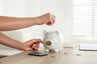 Woman putting money into piggy bank at wooden table indoors, closeup