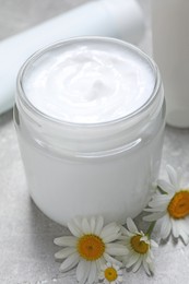 Jar of hand cream and chamomiles on light grey table, closeup