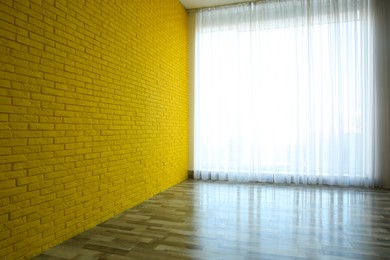 Empty room with yellow brick wall, large window and wooden floor
