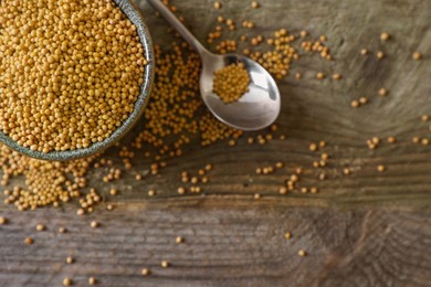 Photo of Bowl and spoon of mustard seeds on wooden table, flat lay. Space for text