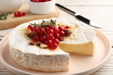 Brie cheese served with almonds, red currants and honey on white wooden table, closeup