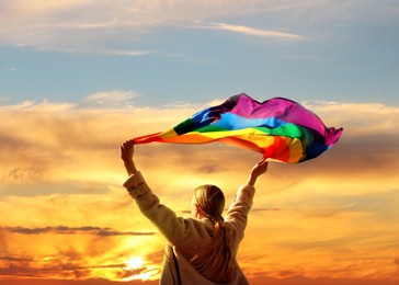 Image of Woman with bright LGBT flag against sky at sunset