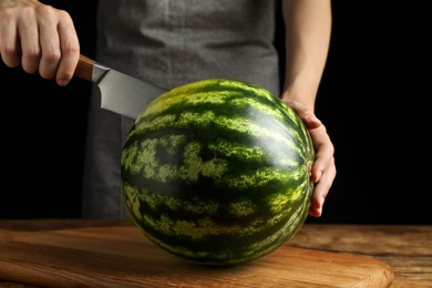 Woman cutting delicious watermelon at wooden table against black background, closeup