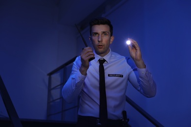Male security guard with flashlight and portable radio transmitter in dark room