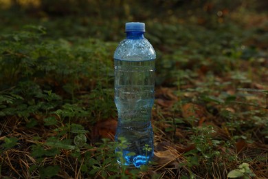 Photo of Plastic bottle of fresh water on green grass outdoors