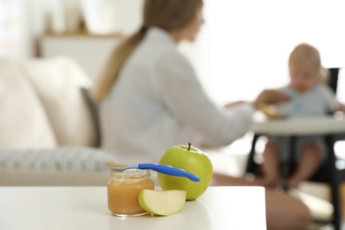 Mother feeding her little baby at home, focus on healthy fruit puree and fresh apples