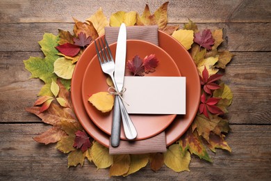 Festive table setting with autumn leaves and blank card on wooden background, flat lay