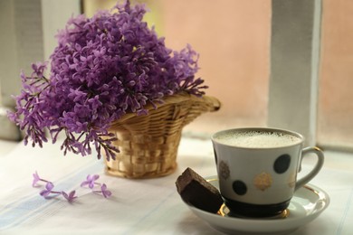 Beautiful lilac flowers, cup of hot coffee and dessert on window sill indoors