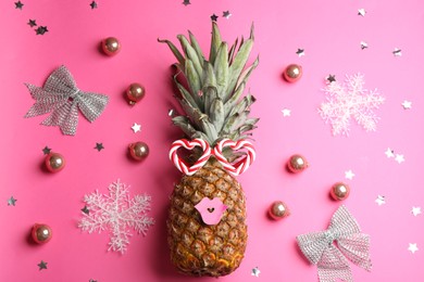 Photo of Pineapple with funny glasses and Christmas decor on pink background, flat lay. Creative concept