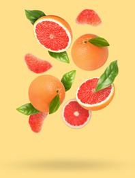 Tasty ripe grapefruits and green leaves falling on beige background