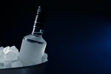 Bottle of vodka in metal bucket with ice on dark background. Space for text