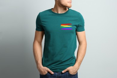 Young man wearing green t-shirt with image of LGBT pride flag on light grey background