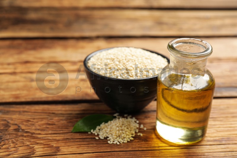 Bottle of sesame oil and seeds on wooden table. Space for text