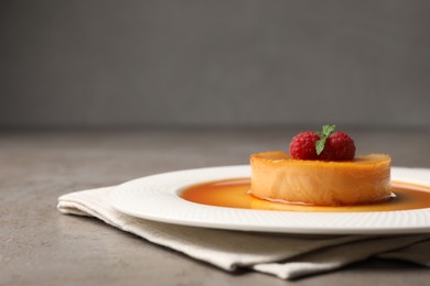 Photo of Delicious pudding with caramel and raspberries on grey table. Space for text