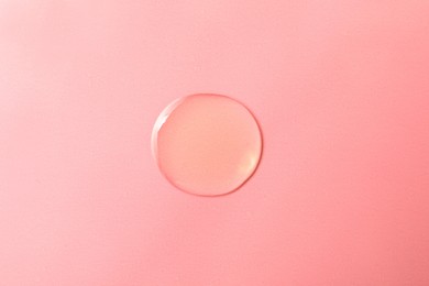 Drop of hydrophilic oil on pink background, top view