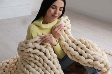 Photo of Young woman with chunky knit blanket on floor at home