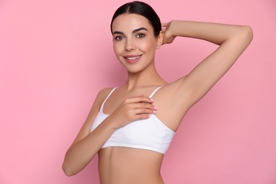 Young woman showing smooth skin after epilation on pink background