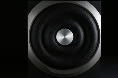 Modern subwoofer on black background, closeup. Powerful audio speaker