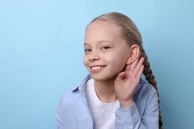 Photo of Cute little girl showing hand to ear gesture on light blue background. Space for text