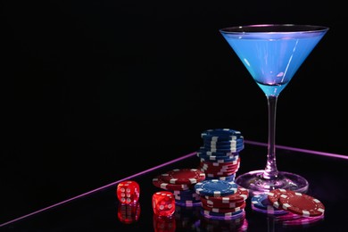 Casino chips, dice and cocktail on dark background, space for text