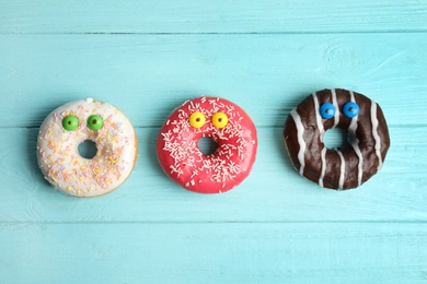 Delicious donuts decorated as monsters on light blue wooden table, flat lay. Halloween treat