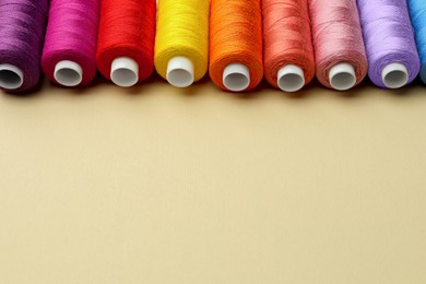 Photo of Set of colorful sewing threads on beige background. Space for text