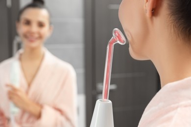 Woman using high frequency darsonval device near mirror in bathroom, closeup. Space for text