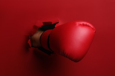 Man breaking through red paper with boxing glove, closeup