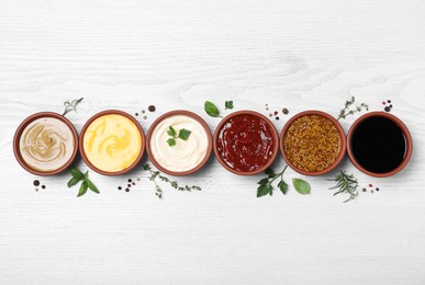 Many different sauces and herbs on white wooden table, flat lay