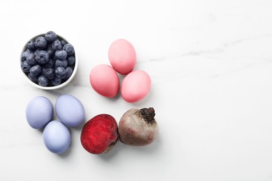 Photo of Colorful Easter eggs painted with natural dyes and ingredients on white marble table, flat lay. Space for text
