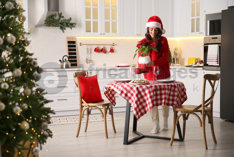 Young woman setting table for Christmas dinner in kitchen
