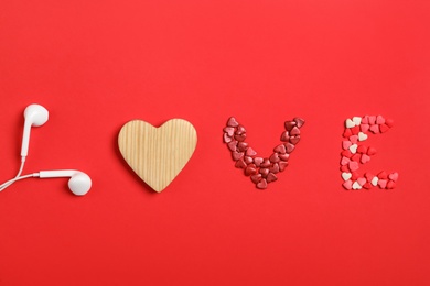 Word Love made with sprinkles, wooden heart and modern earphones on red background, flat lay. Listening music songs