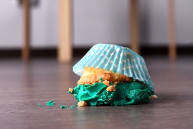 Dropped cupcake with cream on wooden floor at home, closeup. Troubles happen