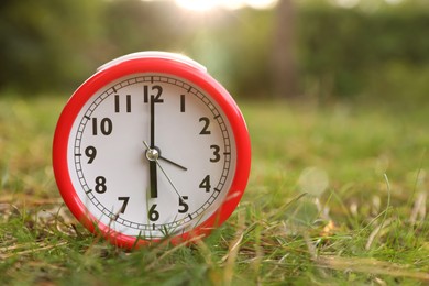 Red alarm clock on green grass outdoors. Space for text