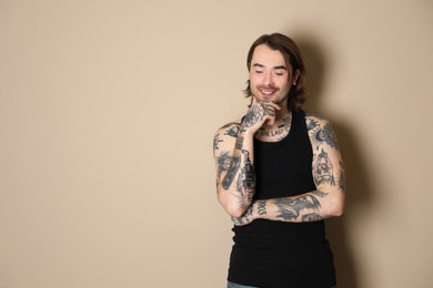 Young man with tattoos on body against beige background. Space for text