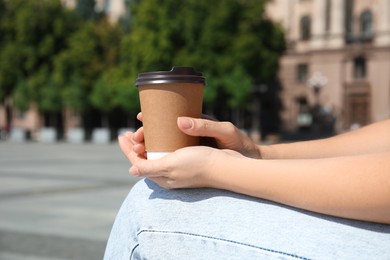 Woman holding takeaway cardboard coffee cup with plastic lid outdoors, closeup