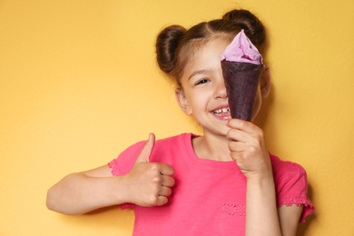 Adorable little girl with delicious ice cream against color background