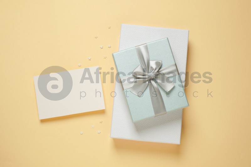 Beautiful gift boxes and blank card on beige background, flat lay. Space for text