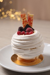 Delicious meringue dessert with berries on table against blurred lights, closeup