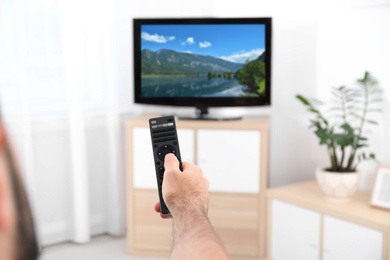 Man switching channels on modern TV with remote control at home
