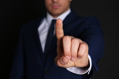 Businessman pointing at something on black background, closeup. Finger gesture