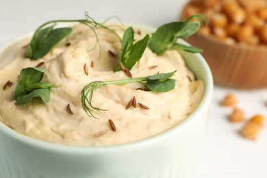 Photo of Bowl of tasty hummus with pea leaves on white table, closeup