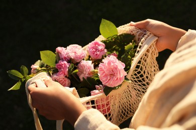 Photo of Woman holding mesh bag with beautiful tea roses outdoors, closeup