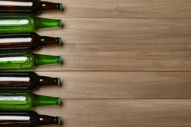 Photo of Glass bottles of beer on wooden background, flat lay. Space for text