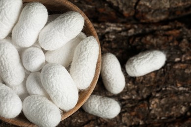 Photo of White silk cocoons with wooden bowl on tree bark, flat lay