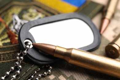 Bullets, military ID tag and Ukrainian patch on pixel camouflage, closeup