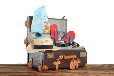 Open vintage suitcase with clothes packed for summer vacation on wooden table against white background