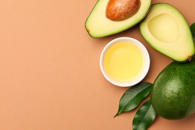 Photo of Cooking oil in bowl and fresh avocados on beige background, flat lay. Space for text
