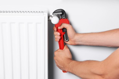Professional plumber using adjustable wrench for installing new heating radiator near white wall, closeup